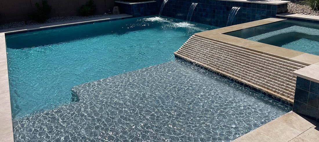 A backyard swimming pool with a cascading waterfall feature and tiled edges.