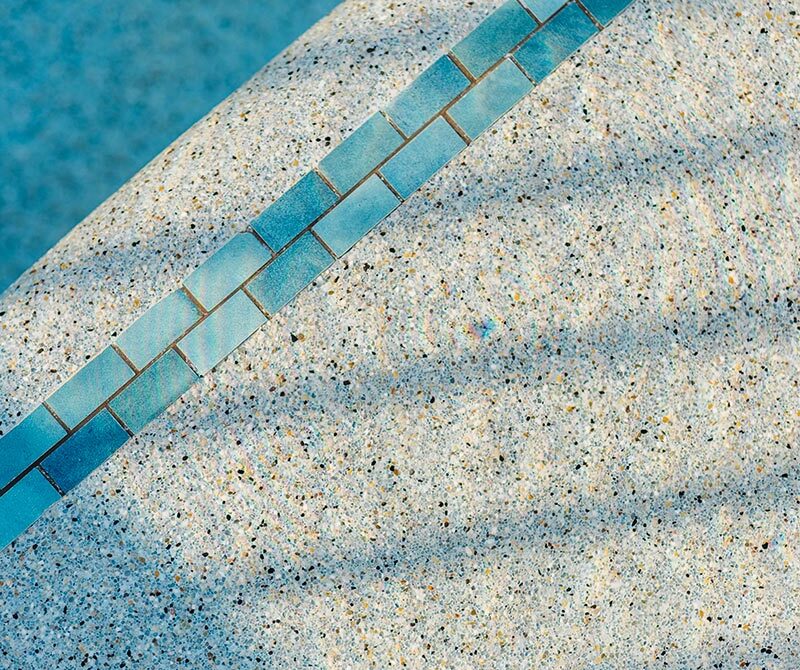 Close-up image of a swimming pool edge with blue tiles and shadow reflections on the adjacent surface.